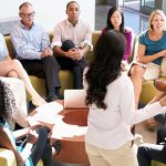 Image of a group of people sitting together in a circle holding a meeting